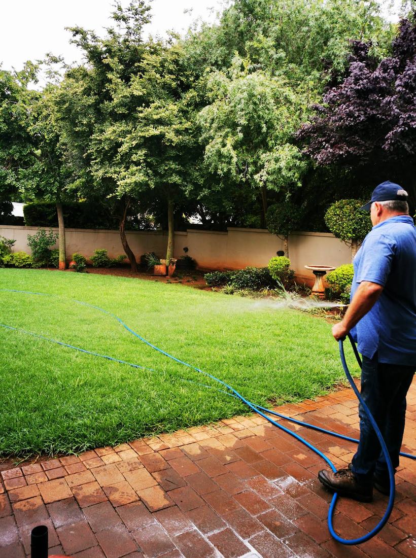 Nico spraying a garden bed along a brick paved path