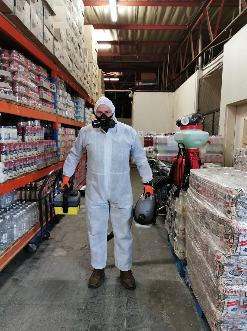 Technician in full protective suit and respirator in a warehouse aisle